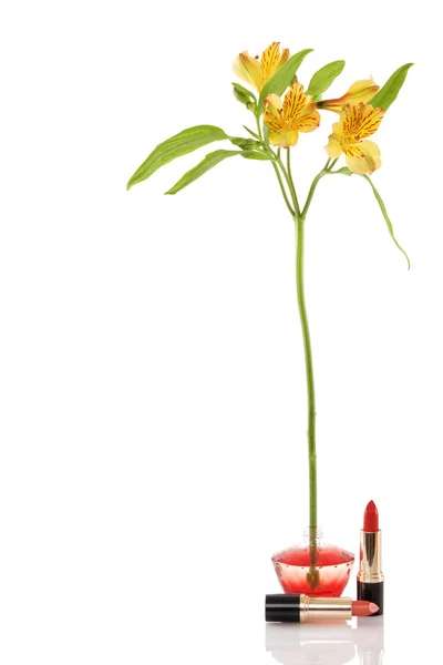 Parfymflaska, gul blomma och två röda läppstift — Stockfoto