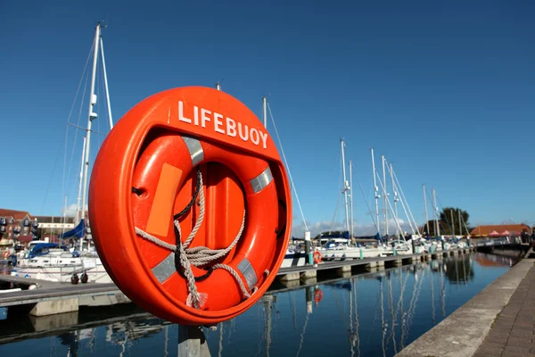 Duże pomarańczowe koło ratunkowe w weymouth harbour z jachtów za — Zdjęcie stockowe
