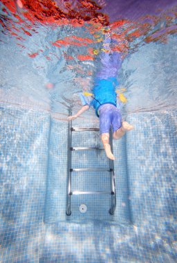 Underwater photo of young boy climbing out of swimming pool clipart