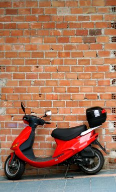 Red moped or motorbike resting or leaning against a brick wall clipart