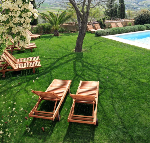 Camas de sol ao lado de uma piscina no jardim — Fotografia de Stock
