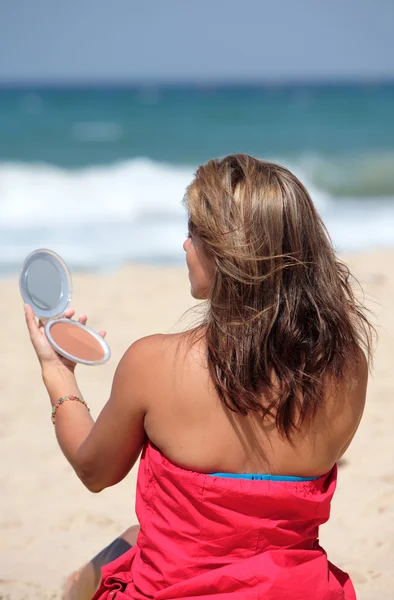 Young tanned woman putting make up on whilst on the beach — Stock Photo, Image