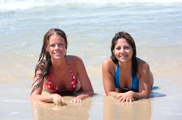 Två vackra unga kvinnor ligger på en solig strand nära vattnet — Stockfoto