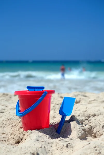 Red bucket and blue spade on sunny sandy beach — Stock Photo, Image