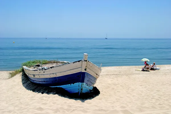 Old rowing boat on white sandy beach and sunbathing next Stock Picture