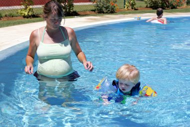 Young boy in buoyancy suit being taught to swim by his pregnant clipart