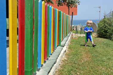 Young boy walking beside colourful fence in the summer clipart