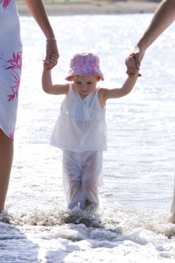 Young girl being walked on beach by parents clipart