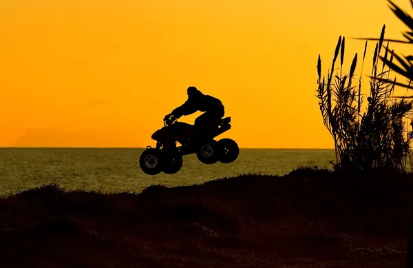 Quad bike jumping na praia ao pôr do sol em Espanha — Fotografia de Stock