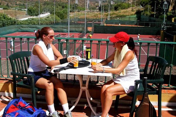 Two women enjoying a cold drink after a game of tennis in the su — Stock Photo, Image