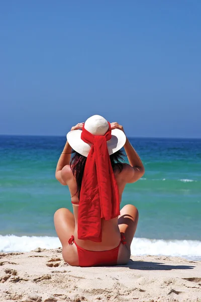 Mädchen sitzt am Sandstrand in der Sonne und justiert ihren Hut. blauer Himmel, — Stockfoto