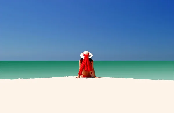 stock image Woman in Red hat and bikini sitting all alone on empty beach