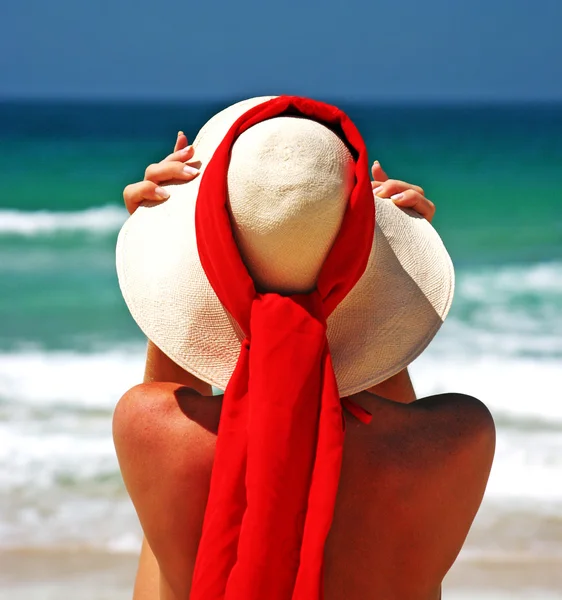 Girl sitting on sandy beach in the sun adjusting hat. Blue sky, — Stock Photo, Image