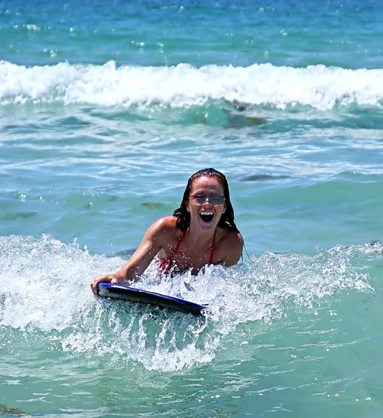 Chica sonriendo mientras monta una gran ola azul en un tablero de cuerpo en el — Foto de Stock
