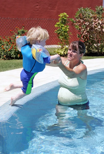 Mãe ajudando seu filho a nadar e saltar em uma piscina ensolarada — Fotografia de Stock
