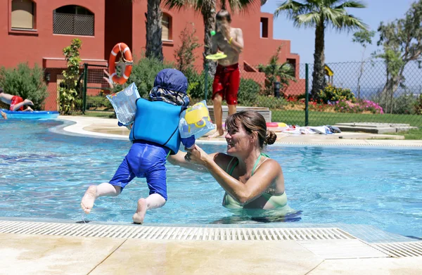 母亲帮她年幼的儿子游泳和跳跃在阳光明媚的 swimmin — 图库照片