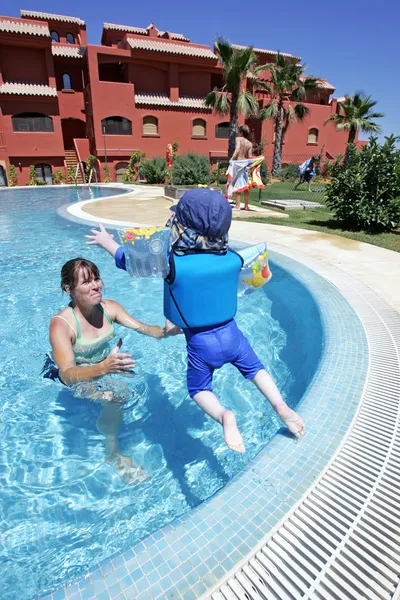 Мама помогает своему маленькому сыну плавать и прыгать в солнечный купальник — стоковое фото