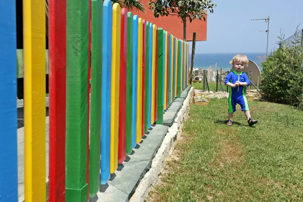 Menino caminhando ao lado de cerca colorida no verão — Fotografia de Stock