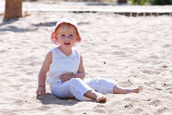 Young child sitting on beach with pink hat — Stock Photo, Image