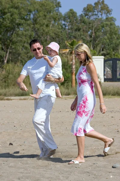 日当たりの良い海岸に沿って歩く若い、健康な家族 — ストック写真