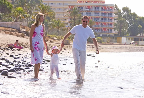 Young, healthy family walking along a sunny beach — Stock Photo, Image