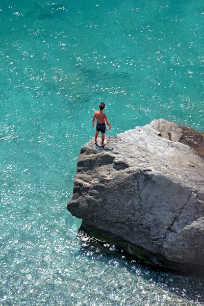 Luftbild eines kleinen Jungen auf einem Felsen, der ins Meer blickt Stockbild