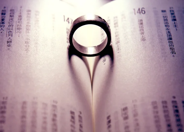 Ring werpt de schaduw van een hart tegen de pagina's van een boek — Stockfoto