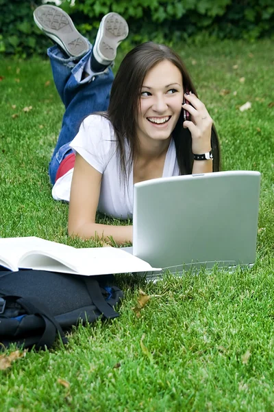 Menina adolescente bonito no telefone deitado na grama estudando — Fotografia de Stock