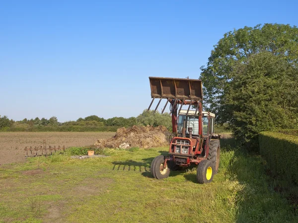 Červený traktor a hnůj haldy — Stock fotografie