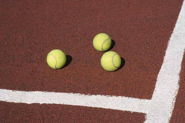 Three tennis balls on brown synthetic court — Stock Photo, Image