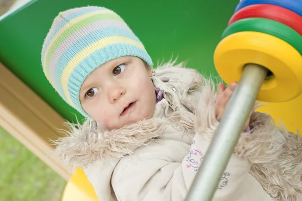 Het meisje in een jas aan een speeltuin — Stockfoto