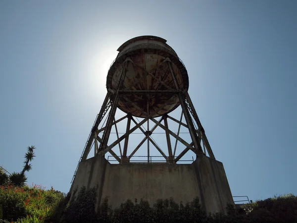 Mirando hacia arriba en la torre de agua oxidada con sol directamente detrás de ella — Foto de Stock
