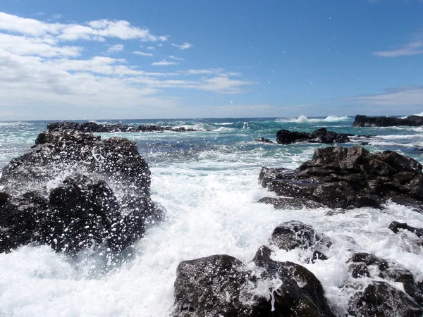Ola se estrella a lo largo de rocas de lava y rocía agua en el aire en r —  Fotos de Stock