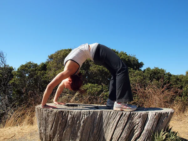 Attractive 20-something lady does a backbend on old tree stump — Stock Photo, Image