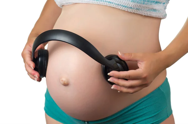 Buik van een zwangere vrouw met hoofdtelefoon. — Stockfoto