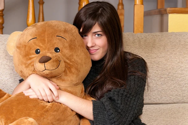 Молода жінка обіймає плюшевого ведмедя, сидячи на дивані крупним планом Стокове Фото