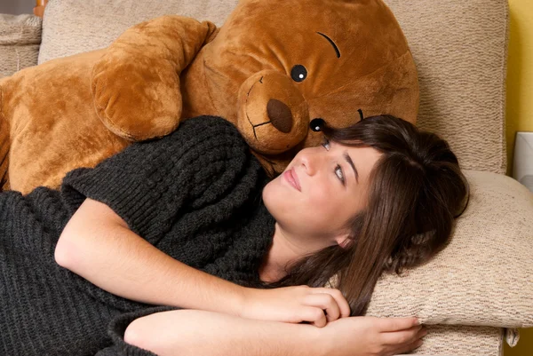Junge Frau umarmt Teddybär, der auf Sofa in Großaufnahme liegt lizenzfreie Stockbilder