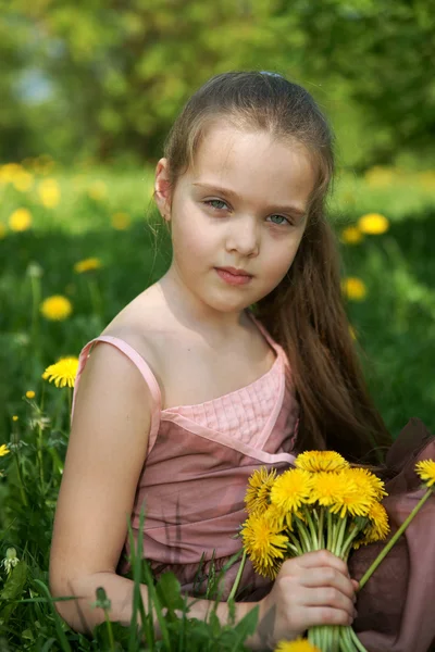 Klein meisje zit op een glade met paardebloemen — Stockfoto