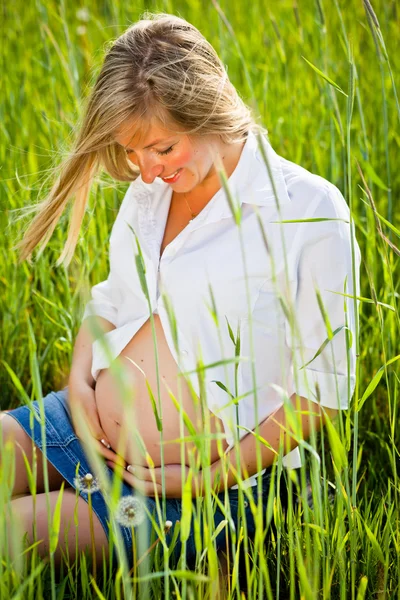 Ciężarna kobieta siedzi na zielone pole — Zdjęcie stockowe