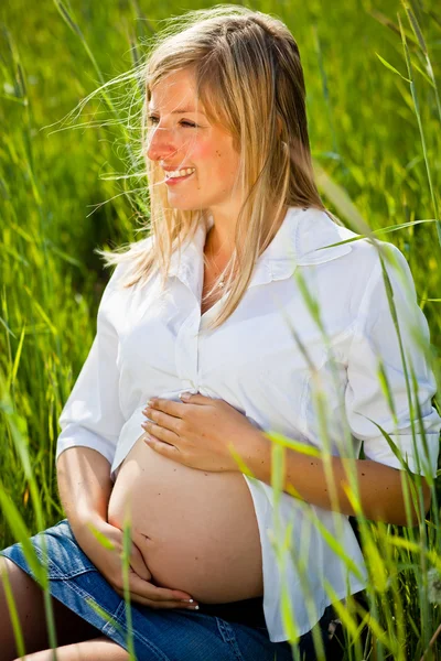 Mujer embarazada sentada en el campo verde — Foto de Stock