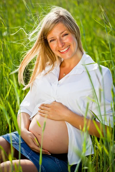 Pregnant woman sitting on green field Stock Picture