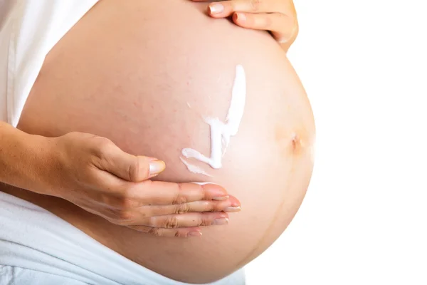 Беременная женщина увлажняет живот, чтобы избежать растяжек, изолированных на белом — стоковое фото