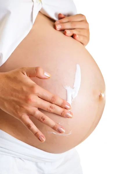 Беременная женщина увлажняет живот, чтобы избежать растяжек, изолированных на белом — стоковое фото