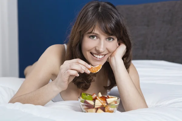Menina na cama comendo frutas — Fotografia de Stock