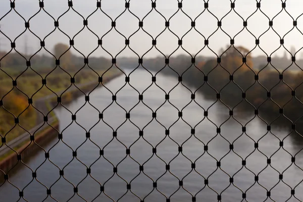 Steel netting in front of blurred river landscape — Stock Photo, Image
