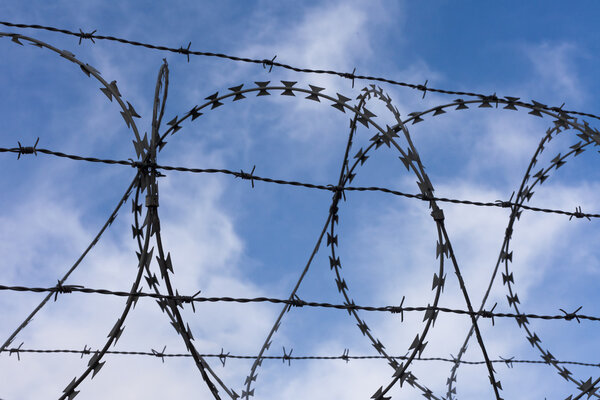 High-security fence with razor and barbed wire before partly clouded blue sky.