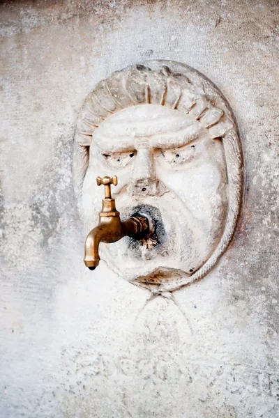 Brass water faucet and carved stone face on wall — Stock Photo, Image