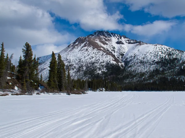 Well used winter trail on frozen mountain lake — Stock Photo, Image