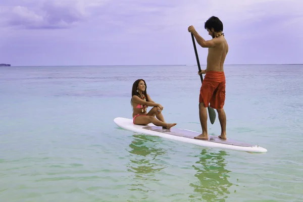 Beachboy med tjej i bikini paddla ombord — Stockfoto