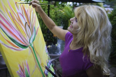 Female artist in her fifties painting on canvas clipart